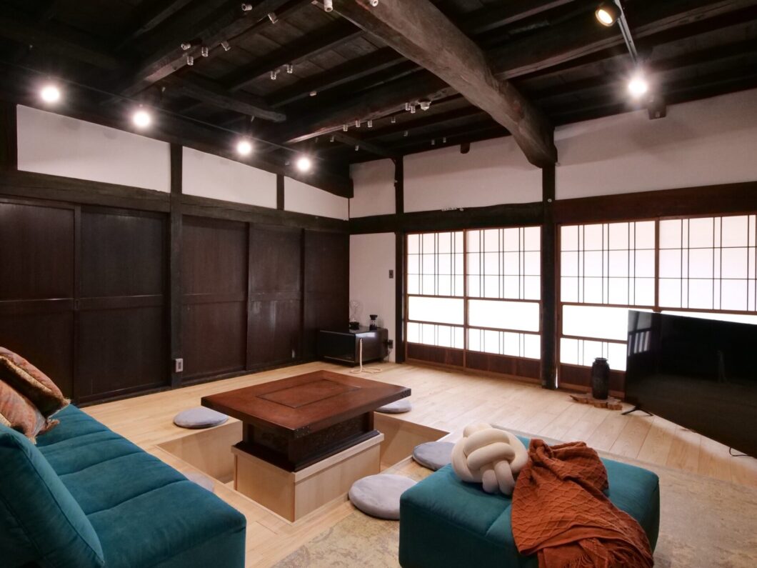 松本市の古民家をリノベーションした和モダンなリビング。天井の梁を活かした開放的な空間に、障子からの柔らかな光が差し込む落ち着いた雰囲気の部屋。